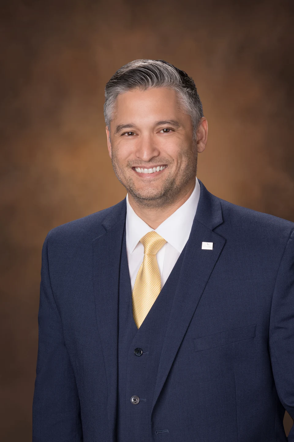 Studio portrait of Jim Butcher in a navy suit and gold tie